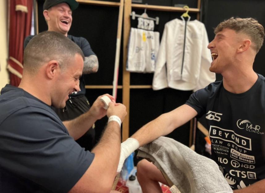 A boxer getting his hands wrapped with two other men laughing in the background.