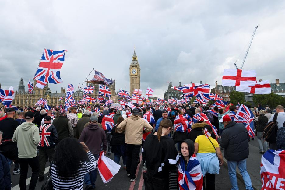 Protesters at an anti-immigration rally in London carrying British flags, with Big Ben in the background.
