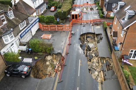Aerial view of two large sinkholes in a residential street, surrounded by safety barriers.