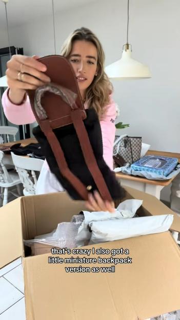 A woman holding up a black miniature backpack with brown leather straps.