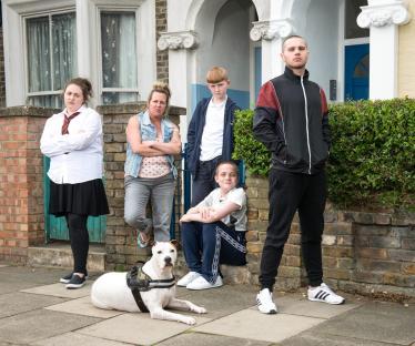 Photo of a family, including a mother and her children, posing outside their home with a dog.