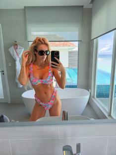 Woman in floral bikini taking a selfie in a bathroom with an ocean view.