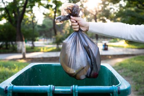 Person throwing a garbage bag into a trash can.
