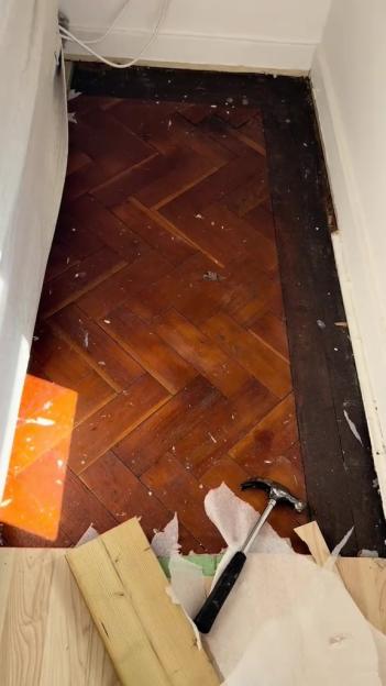 Partially removed flooring revealing original herringbone wood floor.