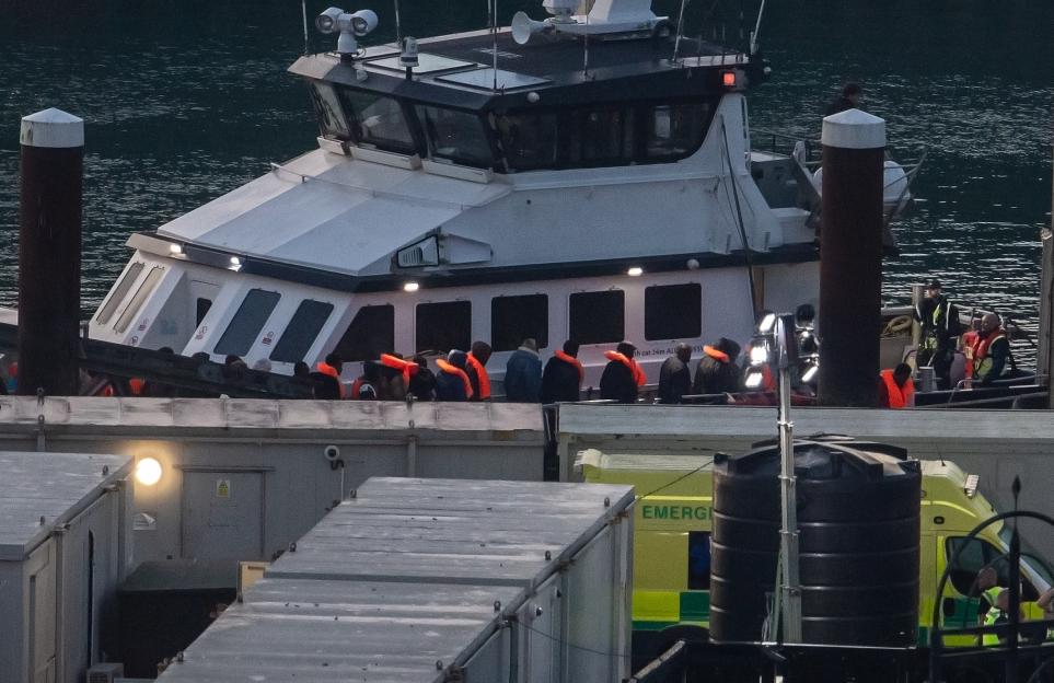 Migrants in orange life vests are escorted off a white Border Force vessel in Dover Docks, Kent.