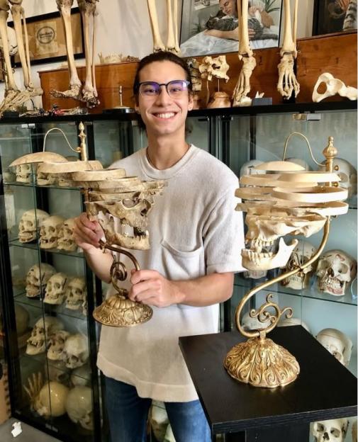 Person holding two skull displays in a room filled with skulls and bones.