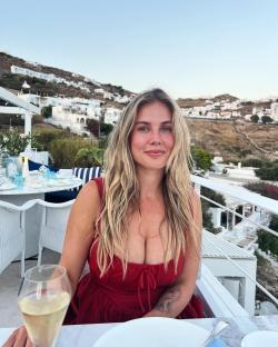 Woman in red dress at outdoor restaurant with seaside view.