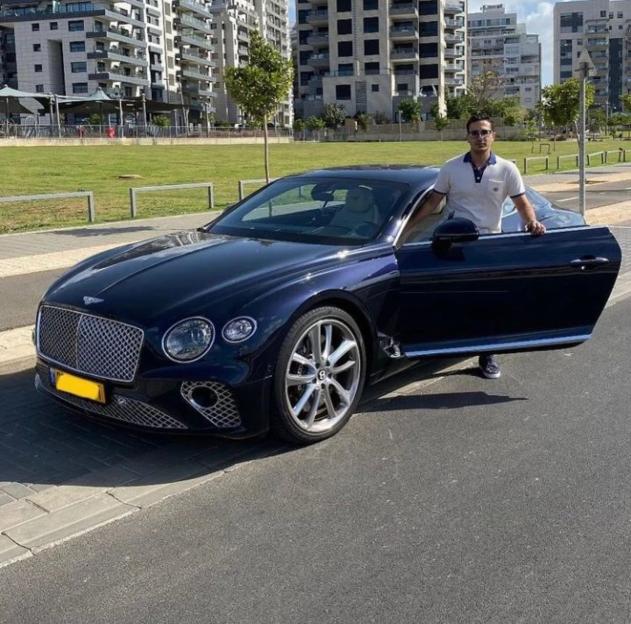 Man standing next to a dark blue Bentley.
