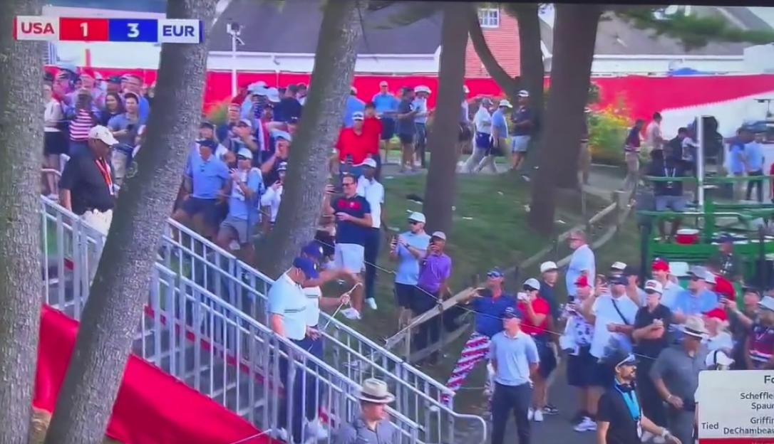 A crowd of spectators at a golf tournament, with a scoreboard in the top left showing USA 1 EUR 3.