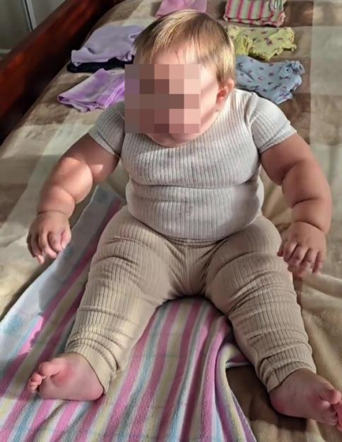 A six-month-old baby sitting on a bed.