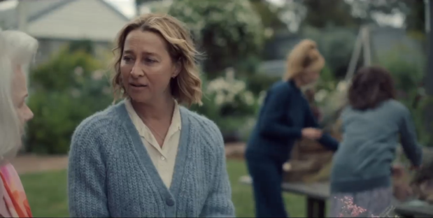 Screenshot of a woman in a blue cardigan talking to an older woman in a garden.