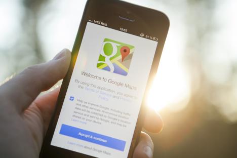 Hand holding iPhone displaying Google Maps welcome screen.