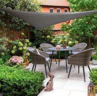 Grey patio furniture set under a grey triangular shade sail in a garden.