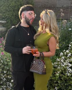 A man and woman playfully sticking out their tongues while holding drinks.