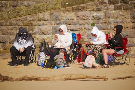 People sitting on chairs on a sandy beach.