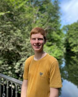 Portrait of a smiling young man with red hair, wearing a mustard-yellow t-shirt, outdoors.