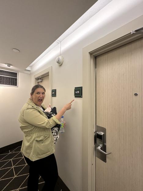 Woman in a hotel hallway holding a baby, pointing to room 428.