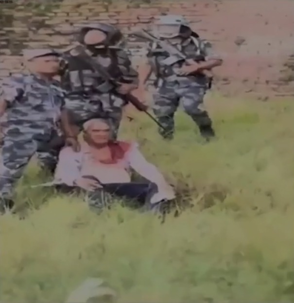 A bloodied man is surrounded by armed guards.