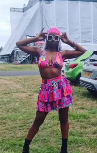 Woman in pink patterned bikini and skirt, wearing sunglasses and headscarf.