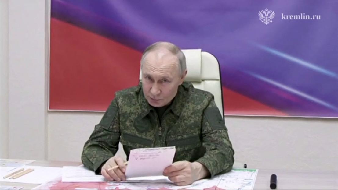 Vladimir Putin in military uniform, holding a note and pencil, at a command point.