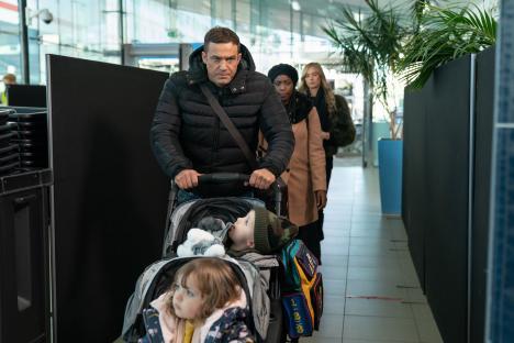 A man pushing a double stroller through an airport terminal, followed by two women.