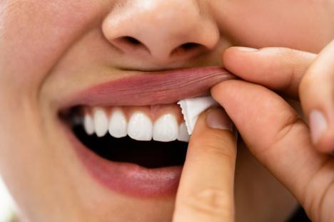 Close-up of a woman using her fingers to remove a piece of wet nicotine pouch from between her teeth.