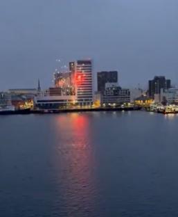 Fireworks over a city waterfront at dusk.