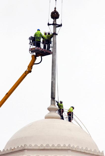 Workers in safety vests and hard hats remove a crown from the top of Wembley Stadium.
