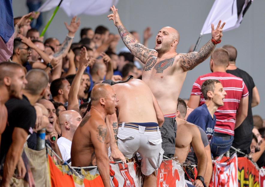 Shirtless, tattooed soccer fans cheering enthusiastically.