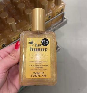 A hand holding a bottle of Hey Hunny Hydrating Body Mist.