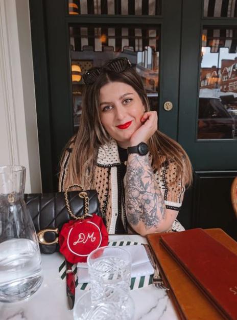 A woman with long hair and a tattooed arm smiling at a restaurant.