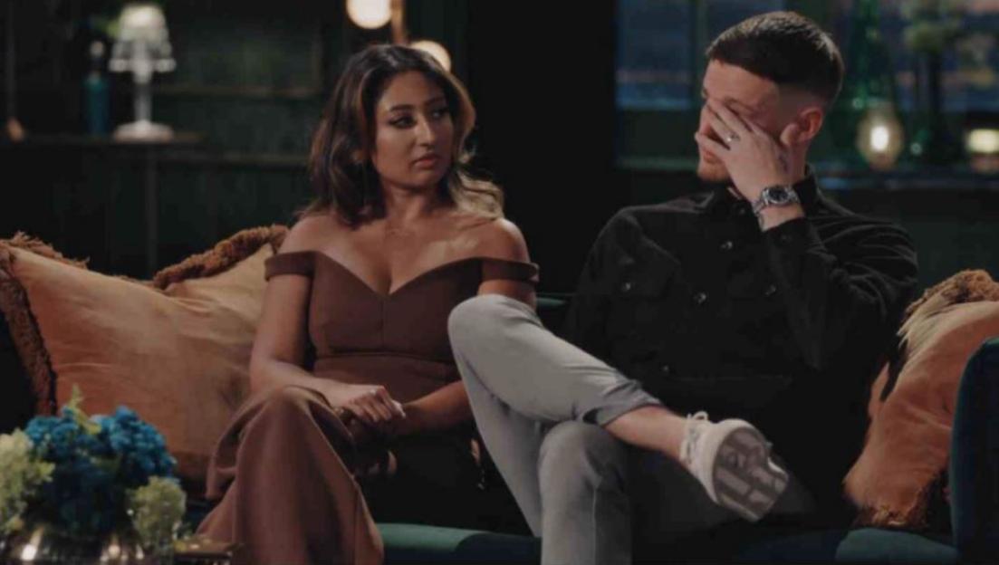 Steven and Nelly sitting on a couch, with Steven rubbing his face and Nelly looking on.