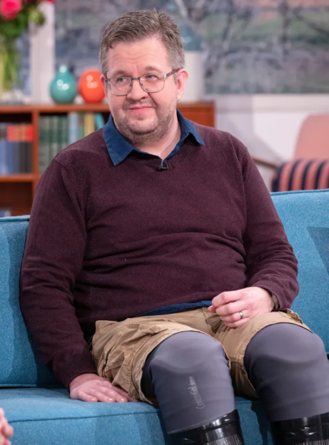 Man sitting on a couch, wearing glasses and a maroon sweater.
