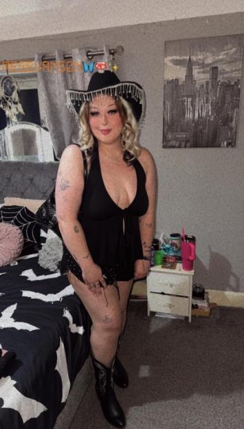 Megan Evanson wearing a black halter top, shorts, cowboy boots, and a black cowboy hat with fringe.