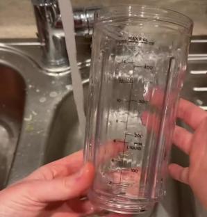 A person rinsing a blender cup in a sink.