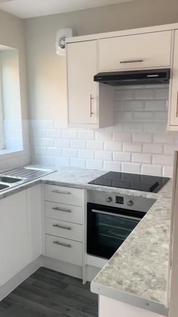 Council-provided kitchen with white cabinets, a tiled backsplash, and a speckled countertop.