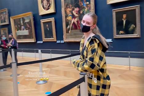 Woman in a yellow and black plaid shirt standing in the Louvre museum.