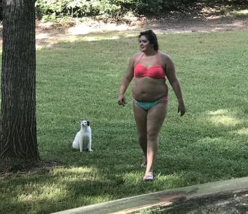 Woman in a bikini walking on a lawn with a cat.