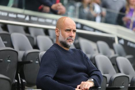 Pep Guardiola sitting in stadium seats.