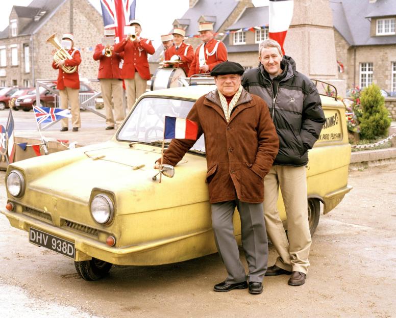 David Jason as Del and Nicholas Lyndhurst as Rodney standing next to a yellow three-wheeled car with a French flag.