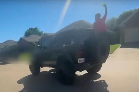 Person standing on the back of a Jeep, holding a water gun.