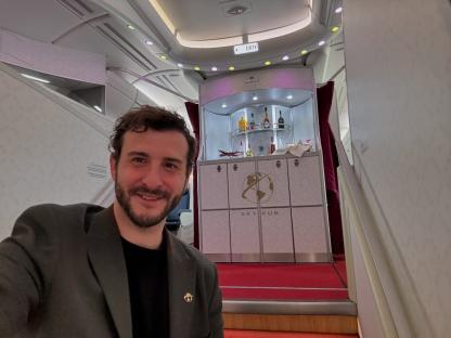 Man in a suit taking a selfie in front of an airplane bar.