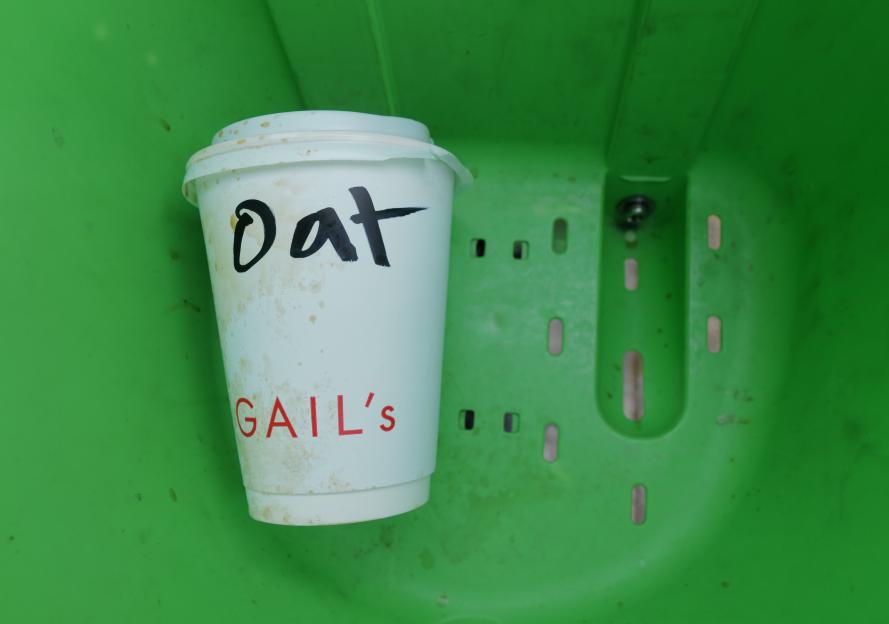 A used Gail's oat milk coffee cup in a green bin.