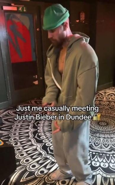 Justin Bieber, with a beard and green beanie, wearing an open hoodie, grey sweatpants, and white sneakers, standing on a patterned floor.