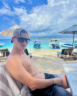 Man relaxing on a beach with boats in the background.
