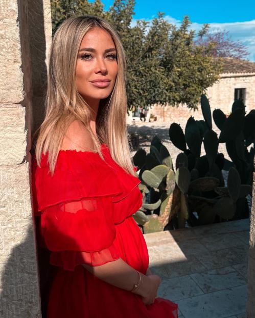 a woman in a red dress leans against a stone wall