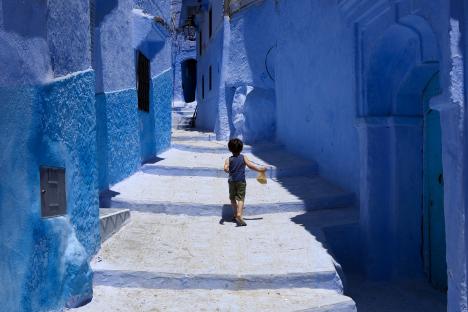 A young boy walks up steps in a blue alleyway in Chefchaouen, Morocco.