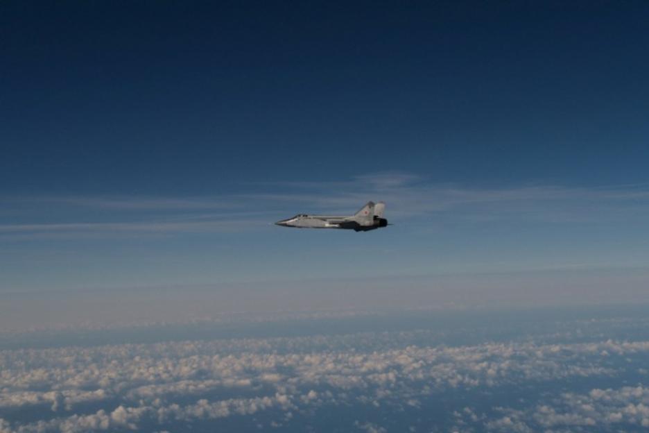 A grey fighter jet flying in the sky above the clouds.