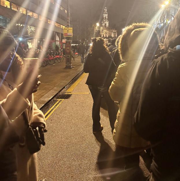 People on a street at night, with a distant building in the background.