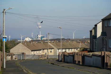 Street scene in Workington, England, showing terraced houses, a factory in the distance, and wind turbines on the horizon.